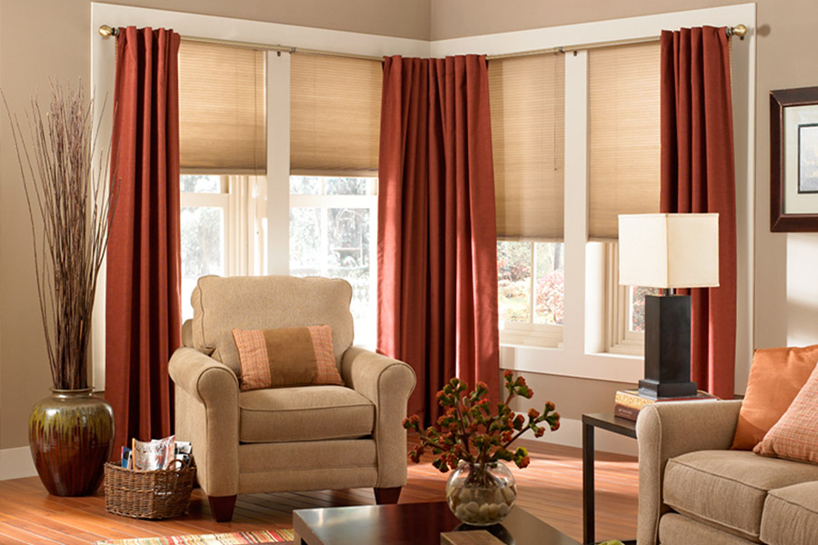 Beige cellular shades with red drapes in a living room corner.